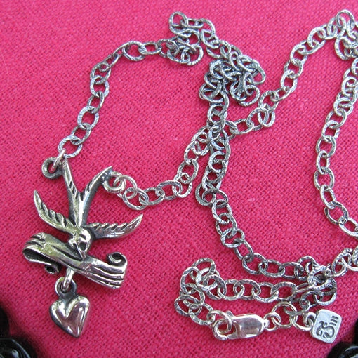 Silver chain necklace with bird and heart charm on a pink background