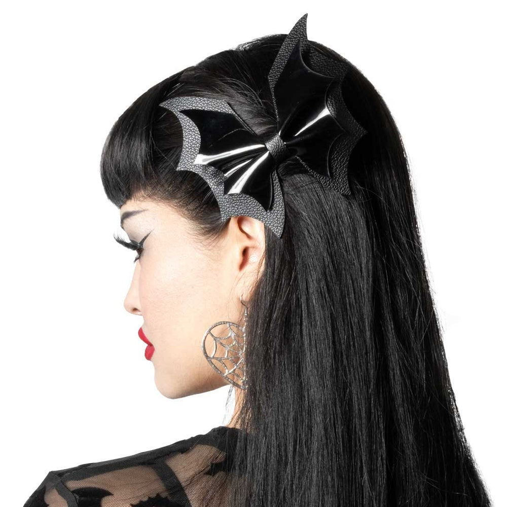 A black bat-wing hair accessory with textured mesh and glossy fabric, shown worn on the side of a model's dark hair against a white background.