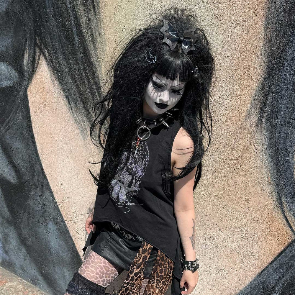 Person with dark hair and gothic makeup against a textured wall.