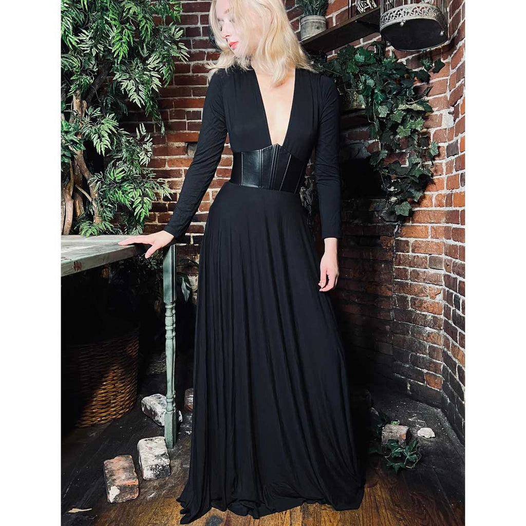 Woman in a black evening gown standing against a brick wall with decorative plants.