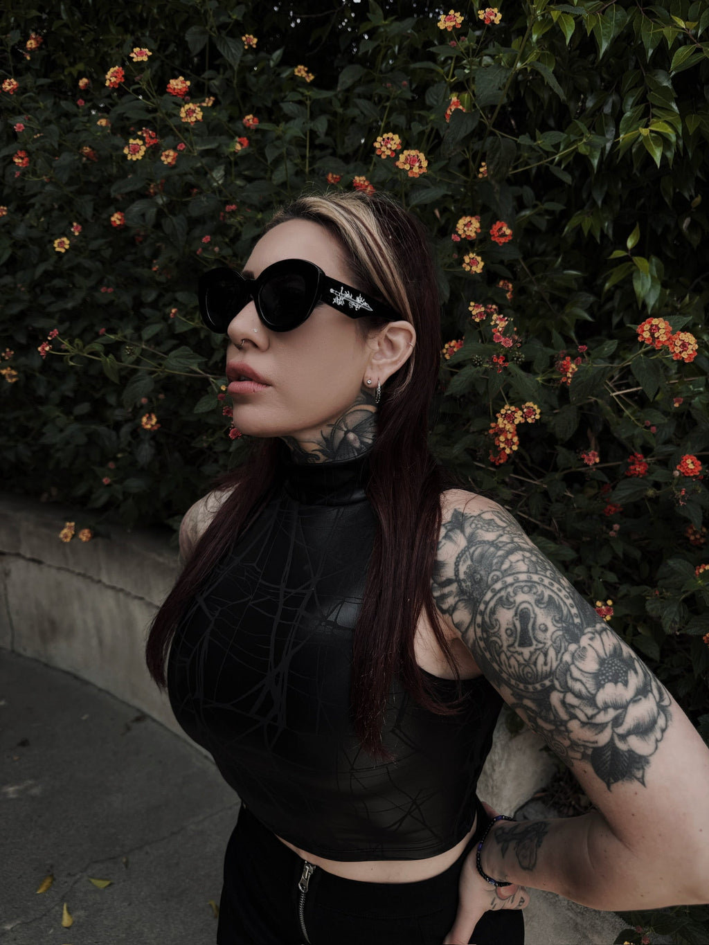 Person with tattoos wearing sunglasses in front of a floral background