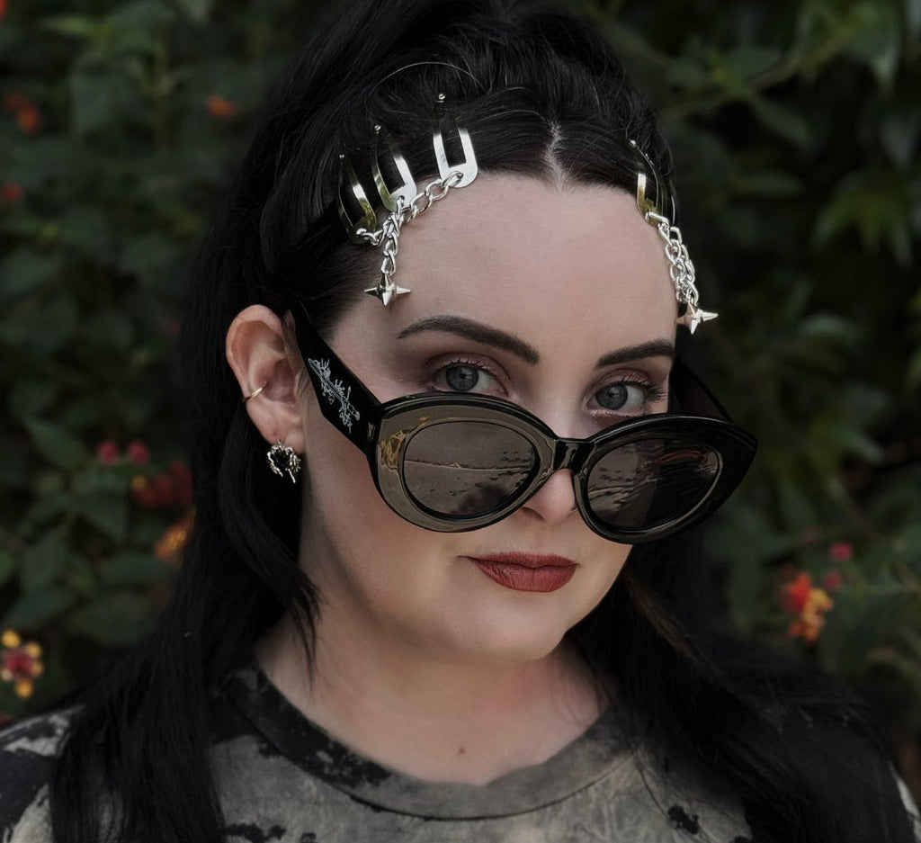 Person with dark hair and sunglasses against a foliage background