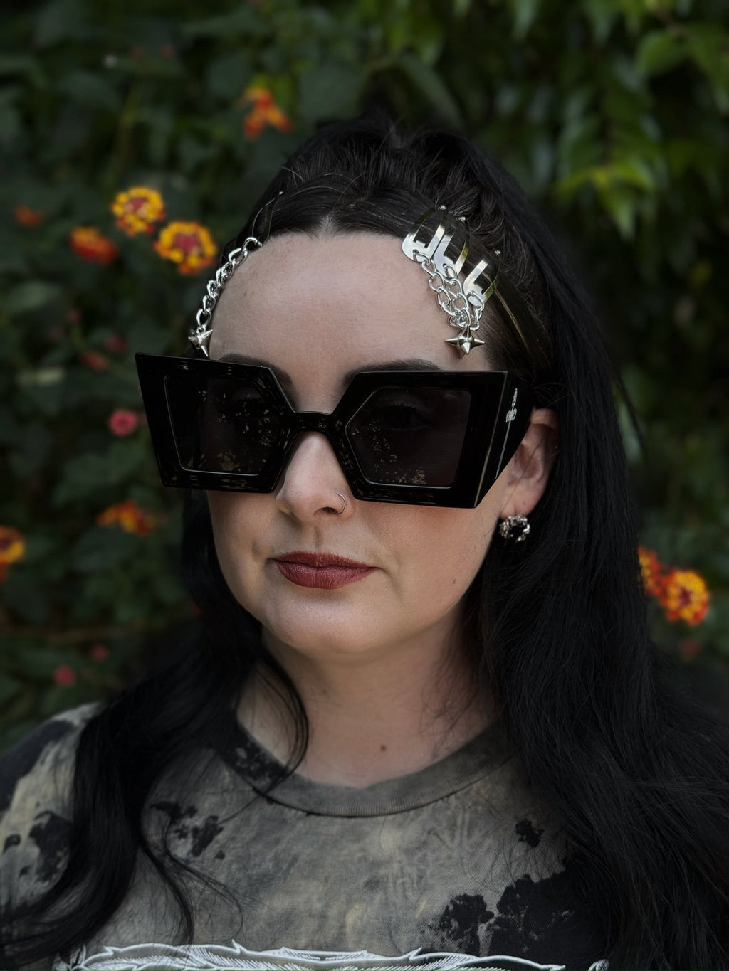 Person wearing black sunglasses and a decorative headpiece with a blurred natural background