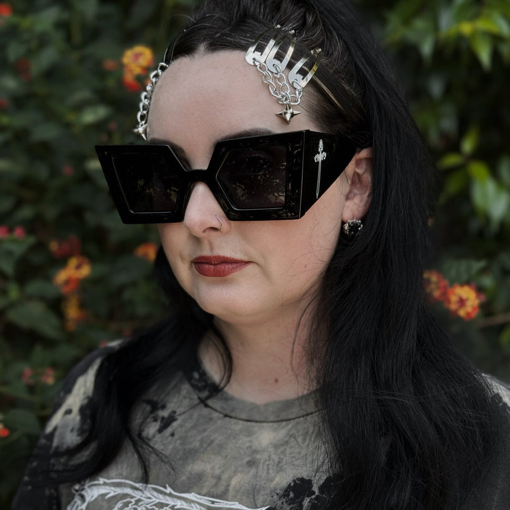 Person wearing large black sunglasses with a floral headband against a green leafy background