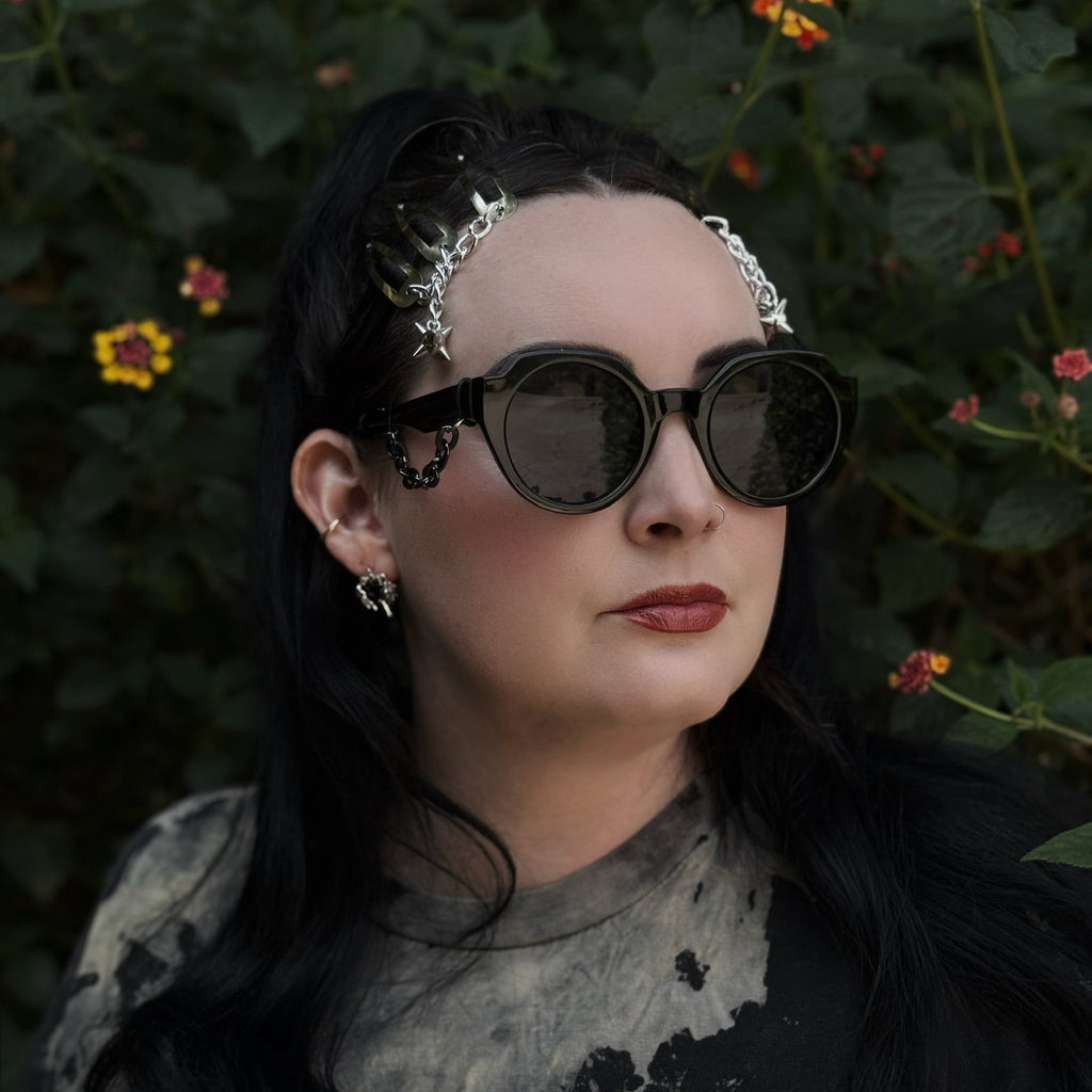 Person wearing sunglasses with a dark background and flowers