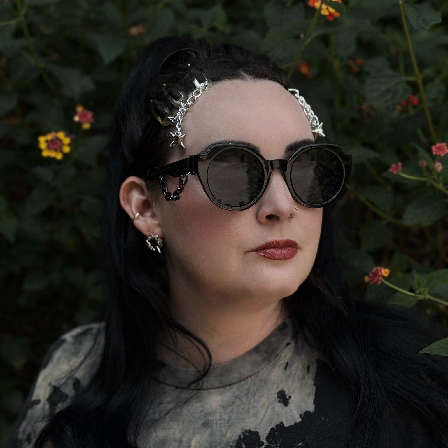 Person wearing sunglasses with a dark background and flowers