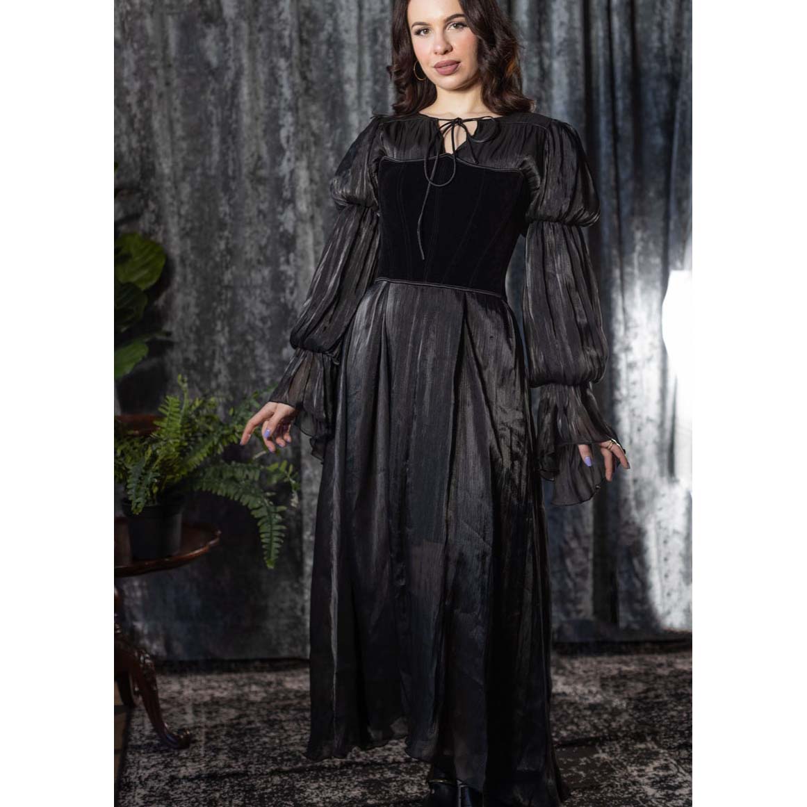 Woman wearing a dark, long-sleeve dress with a black top against a textured wall.