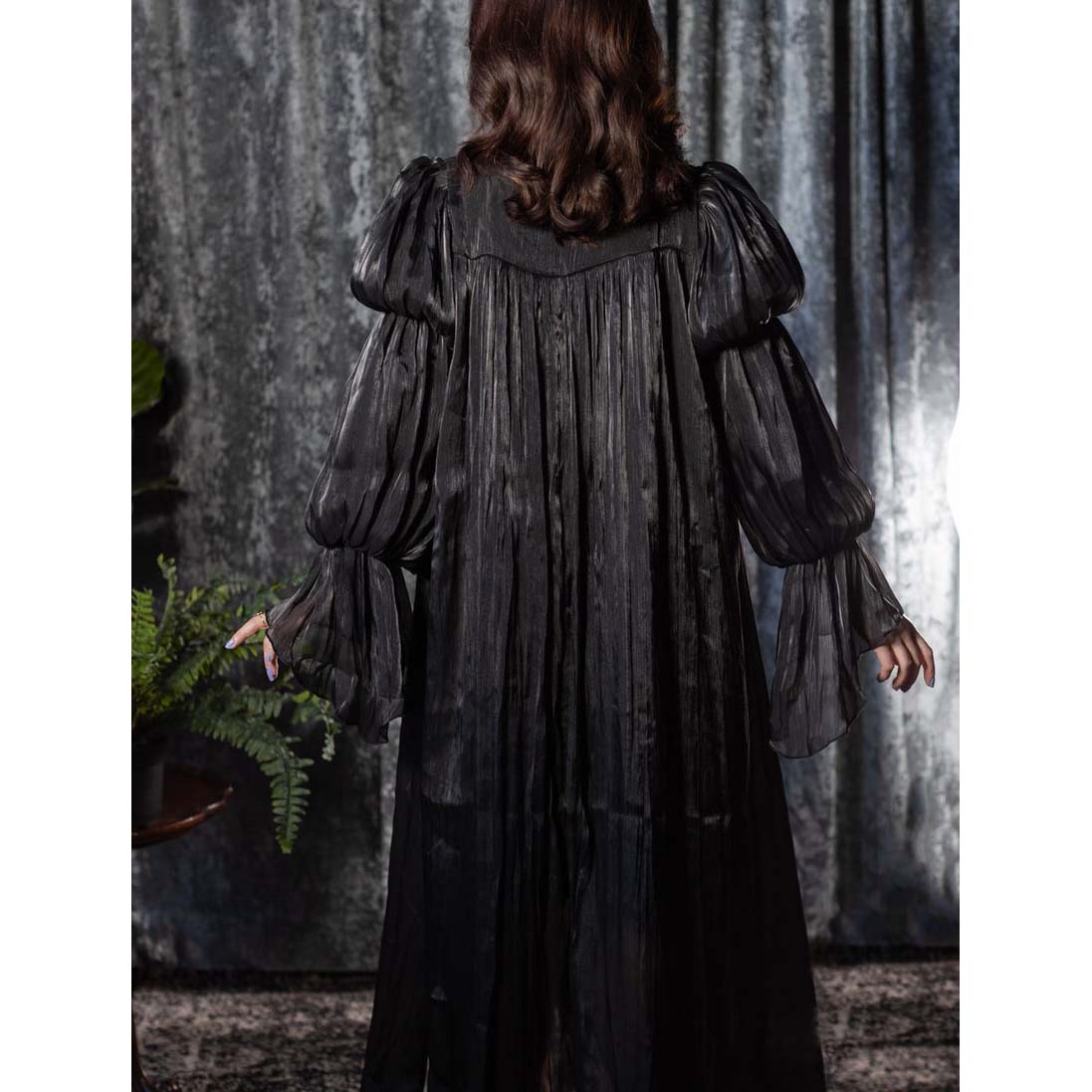 Person wearing a dark, long-sleeve dress with a textured pattern against a gray curtain background.