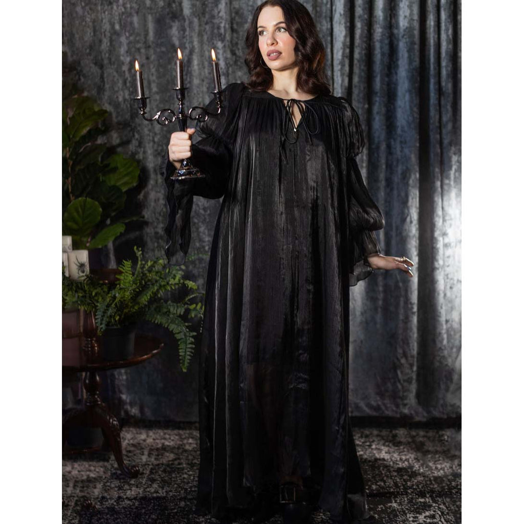 Woman in a long black dress holding a candelabrum in a dark, moody setting.