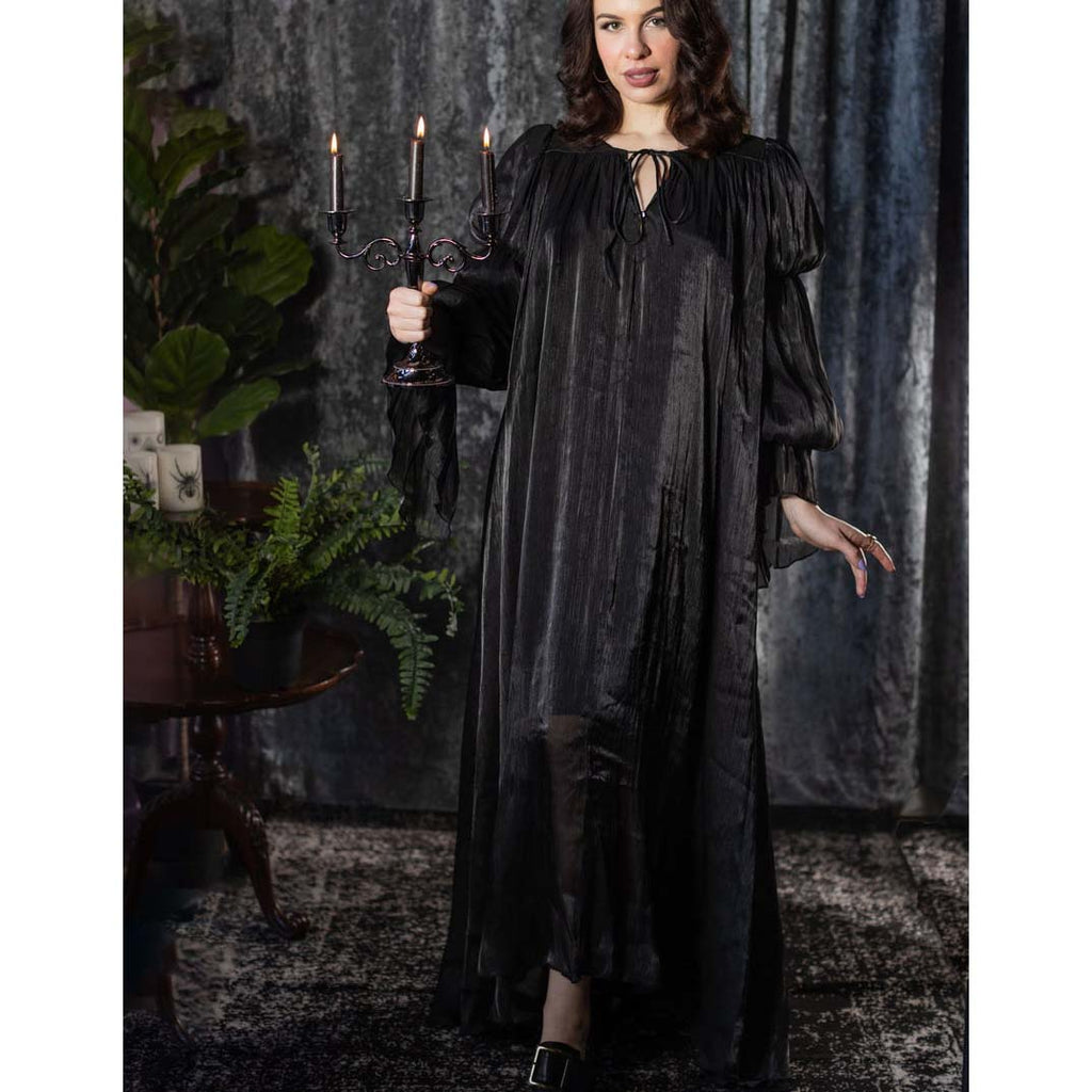 Woman in a long black dress holding a candlestick with candles against a dark, textured wall.