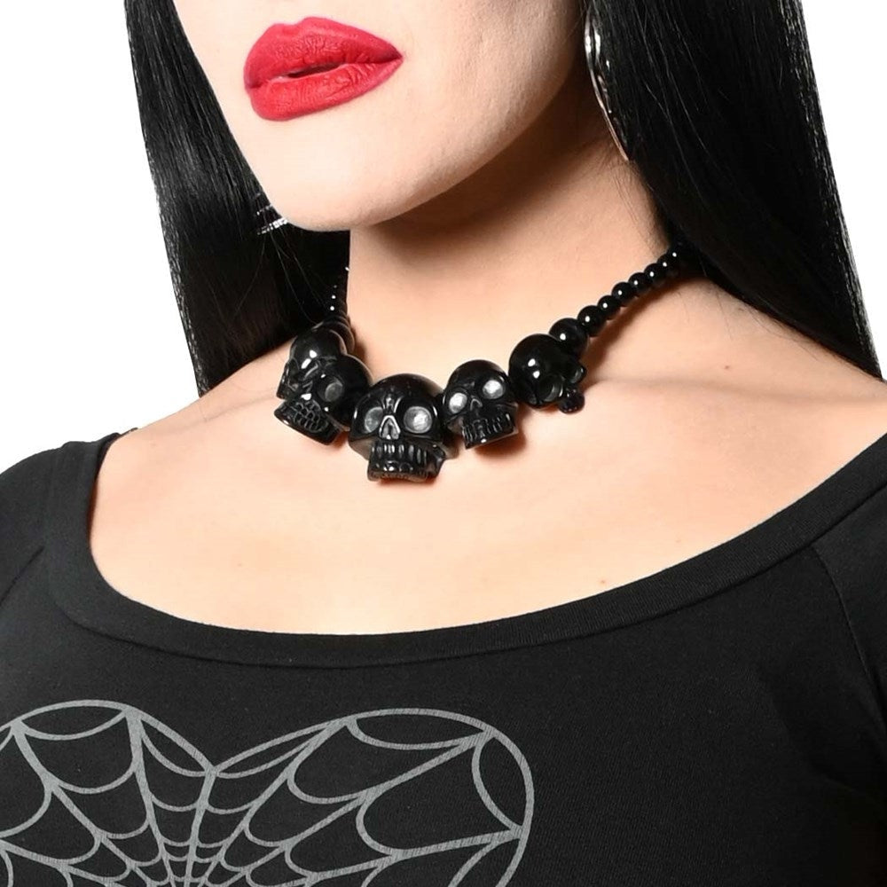 Black skull necklace worn by a person with red lipstick on a white background