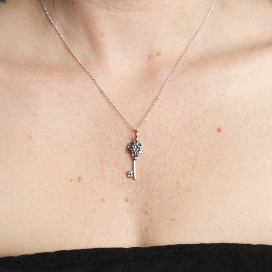 Person with tattoos on arms and chest wearing a necklace with a key pendant.