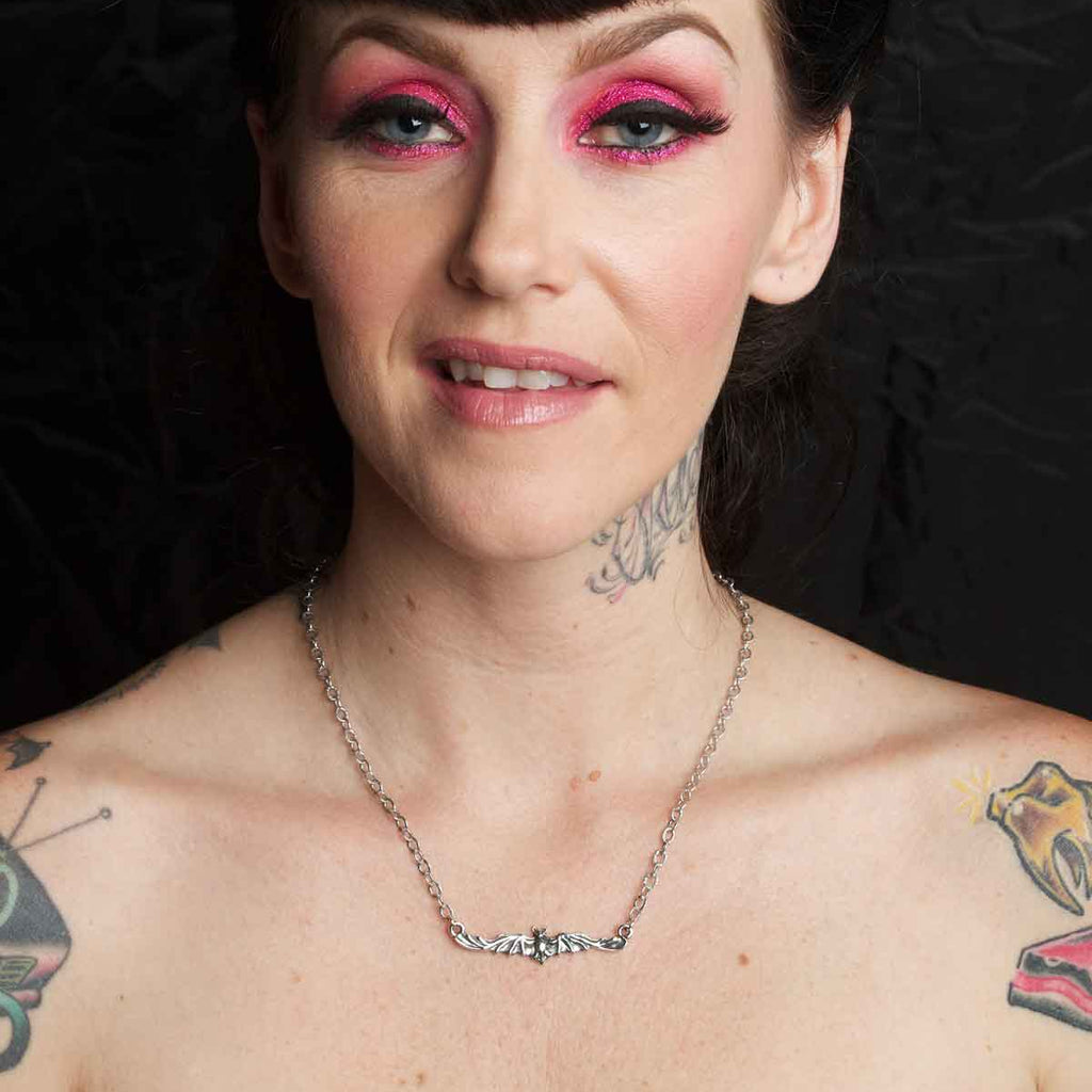 Woman with tattoos and pink eye makeup against a black background