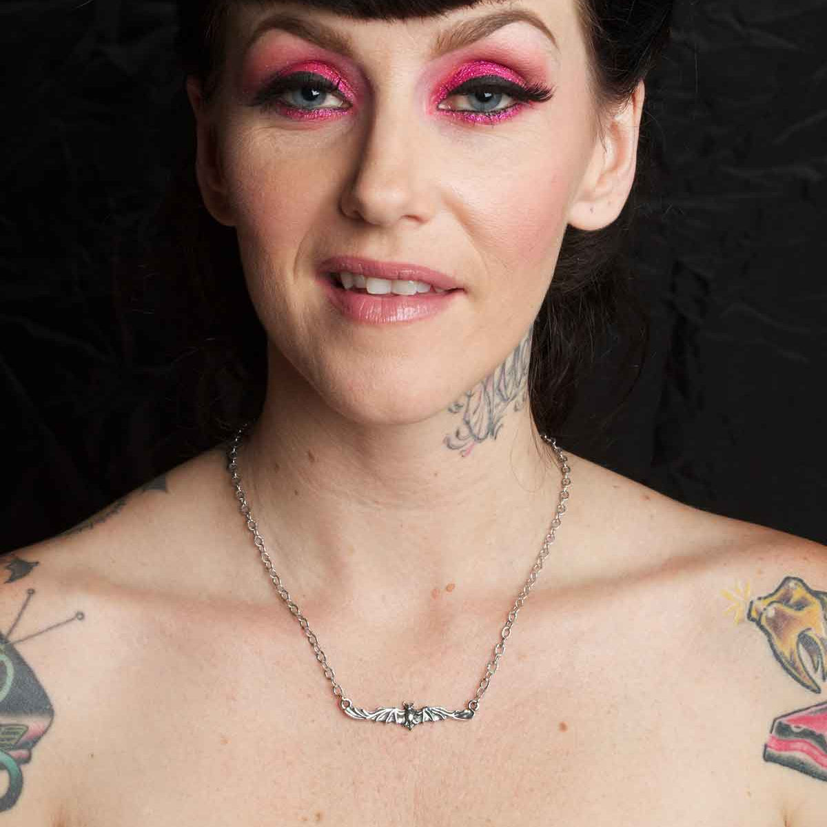 Woman with tattoos and pink eye makeup against a black background