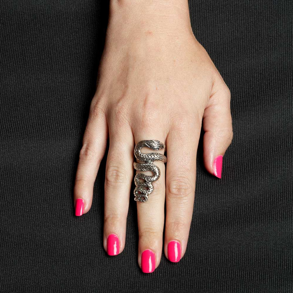 Hand wearing a silver snake-shaped ring with pink nail polish on a black background
