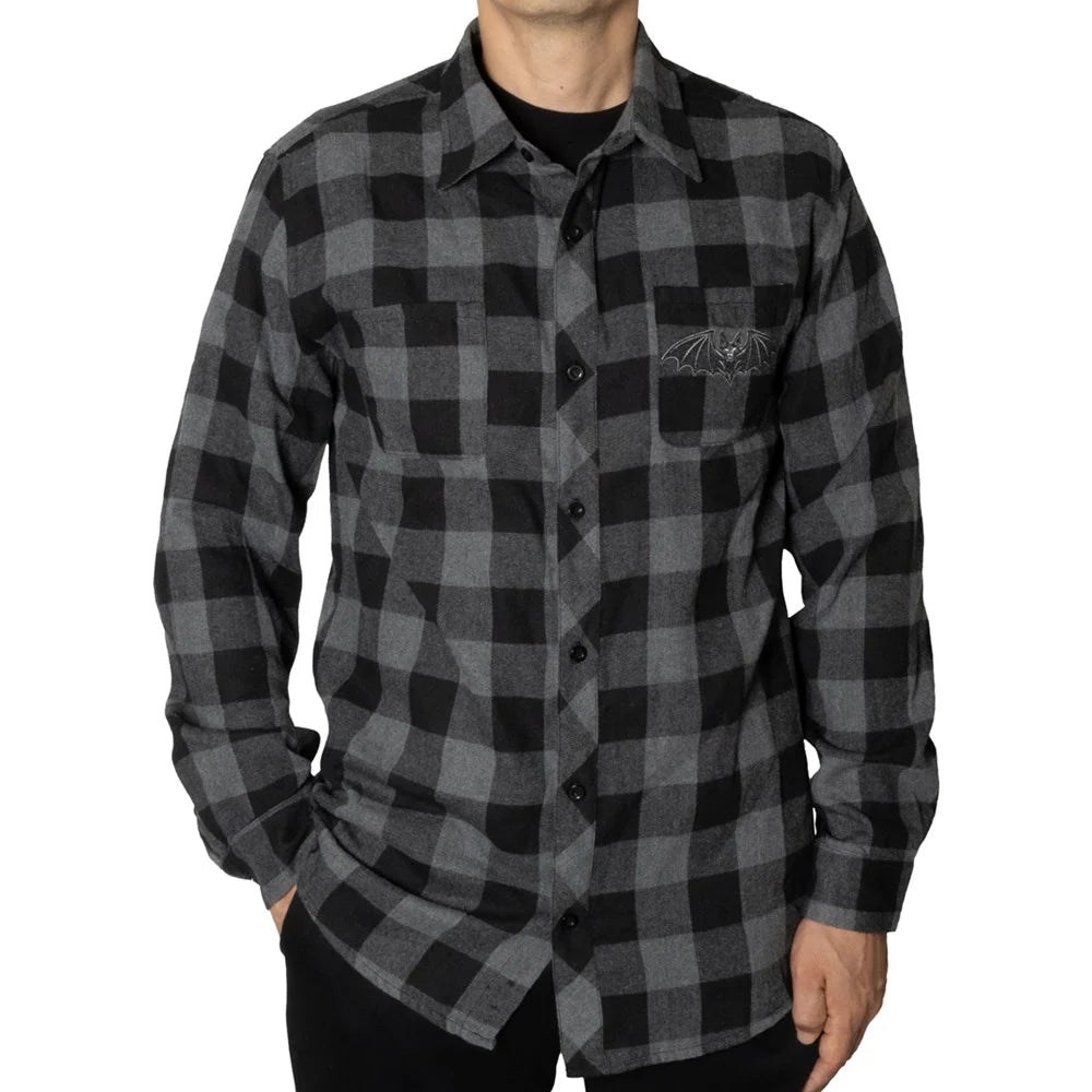 A man wearing a long-sleeve black and gray buffalo plaid button-up shirt with a chest pocket featuring a dark embroidered logo, photographed against a plain white background.