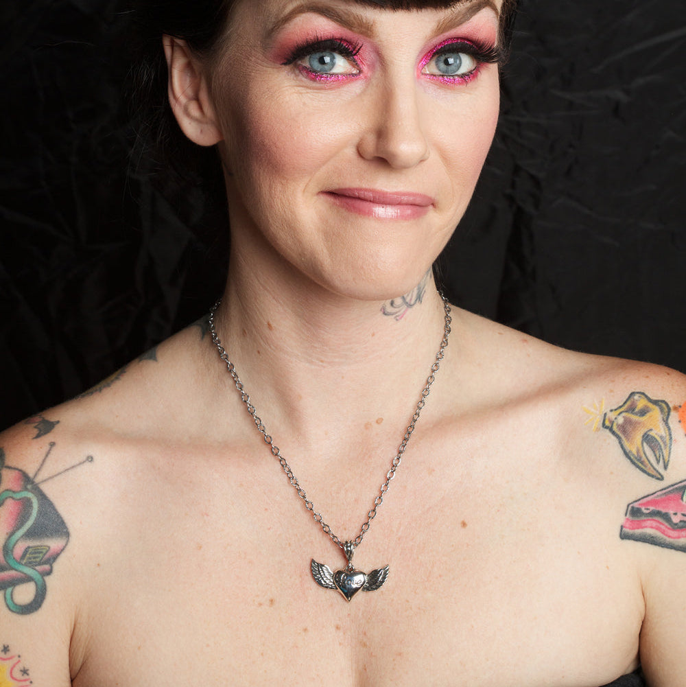 Person with tattoos and colorful makeup wearing a black top against a dark background