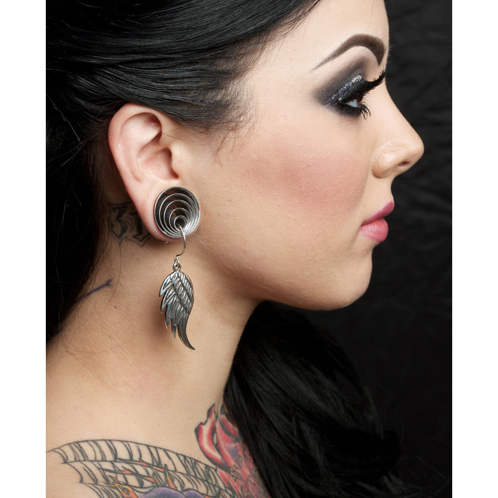 Close-up of a woman wearing a silver earring with a feather design, against a neutral background.