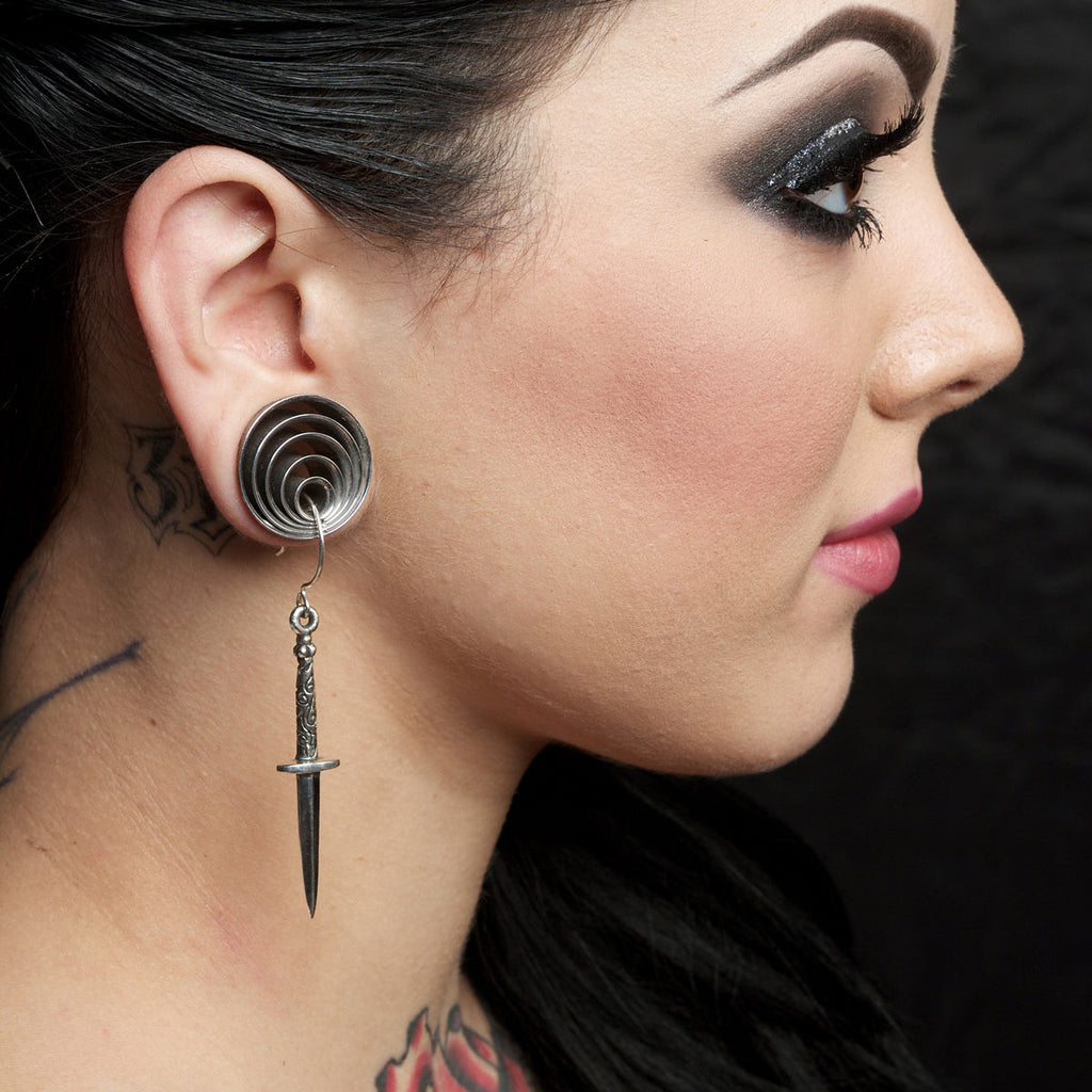 Close-up of a woman's profile wearing a unique earring with a dagger design.