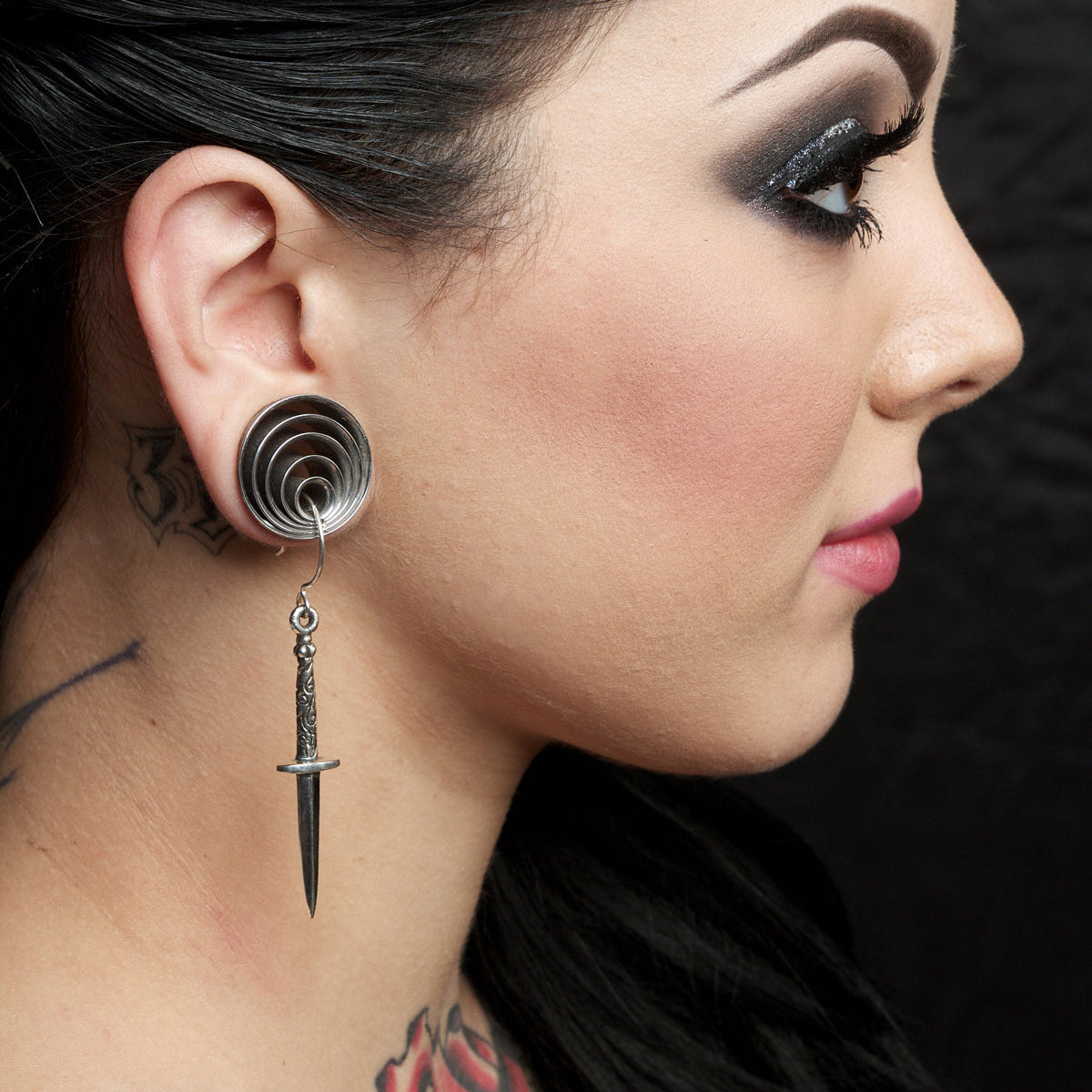 Close-up of a woman's profile wearing a unique earring with a dagger design.