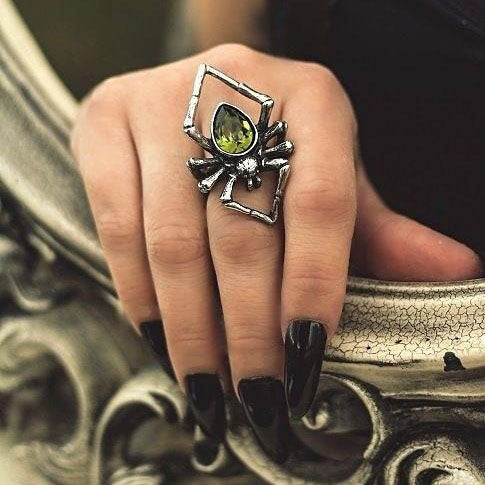 Silver spider ring with green gemstone on a hand with black nail polish.