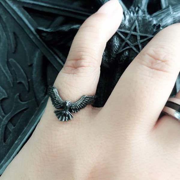 Silver raven ring on a person's finger with a dark background