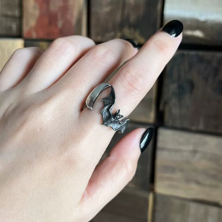 Hand wearing a silver bat-shaped ring with black nail polish on a tiled background