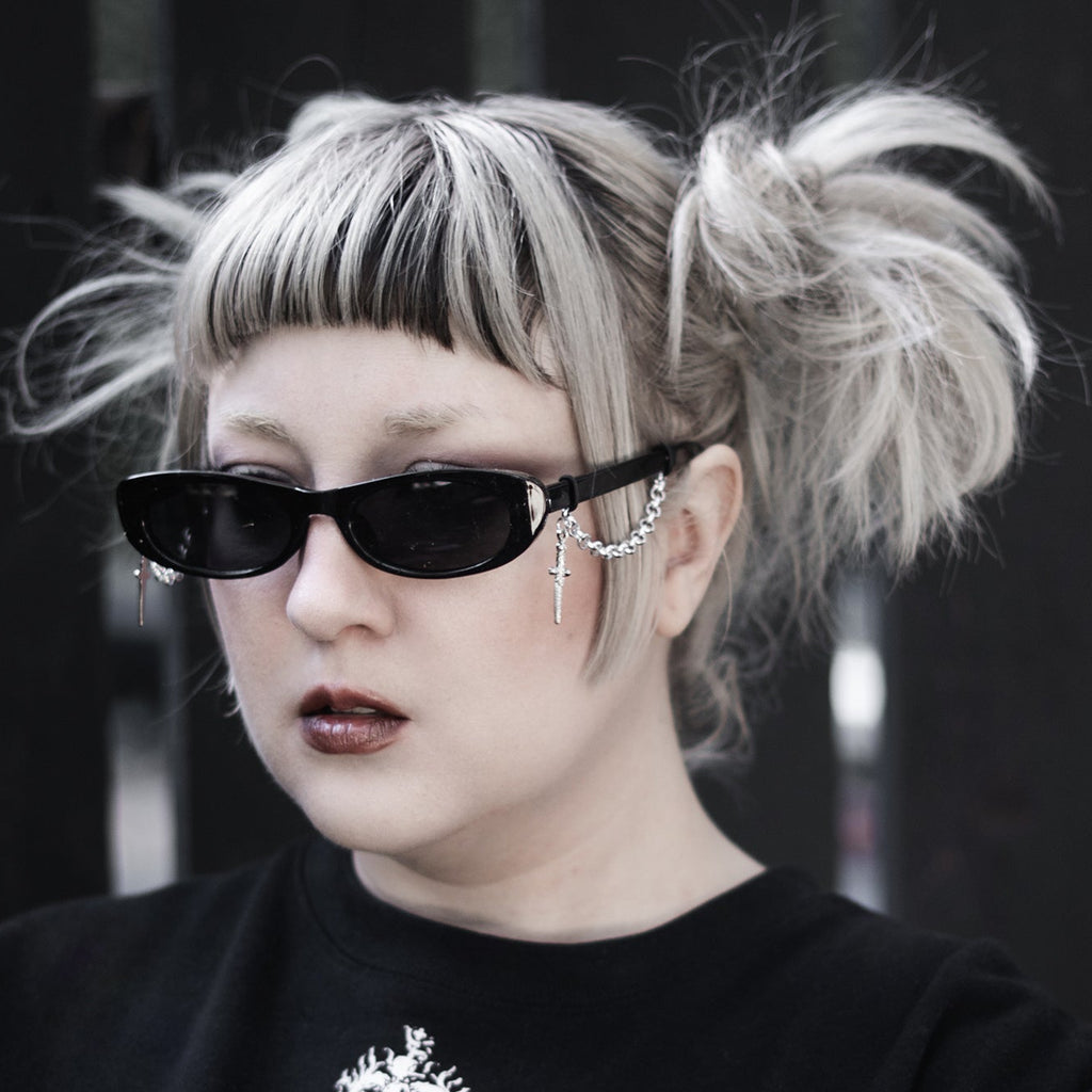 Person with styled hair and dark sunglasses wearing a black sweater with a heart design.