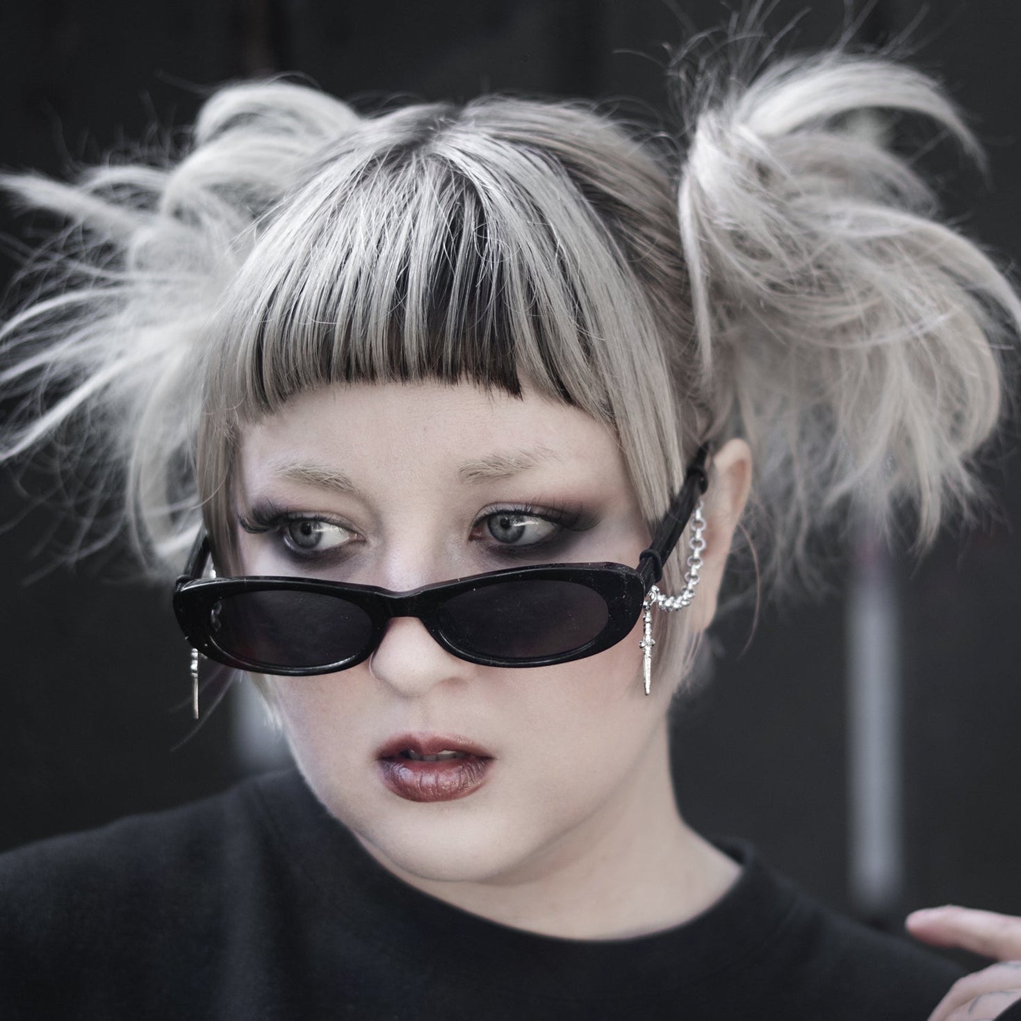 Person with styled hair and dark sunglasses wearing a black sweatshirt with a heart design.
