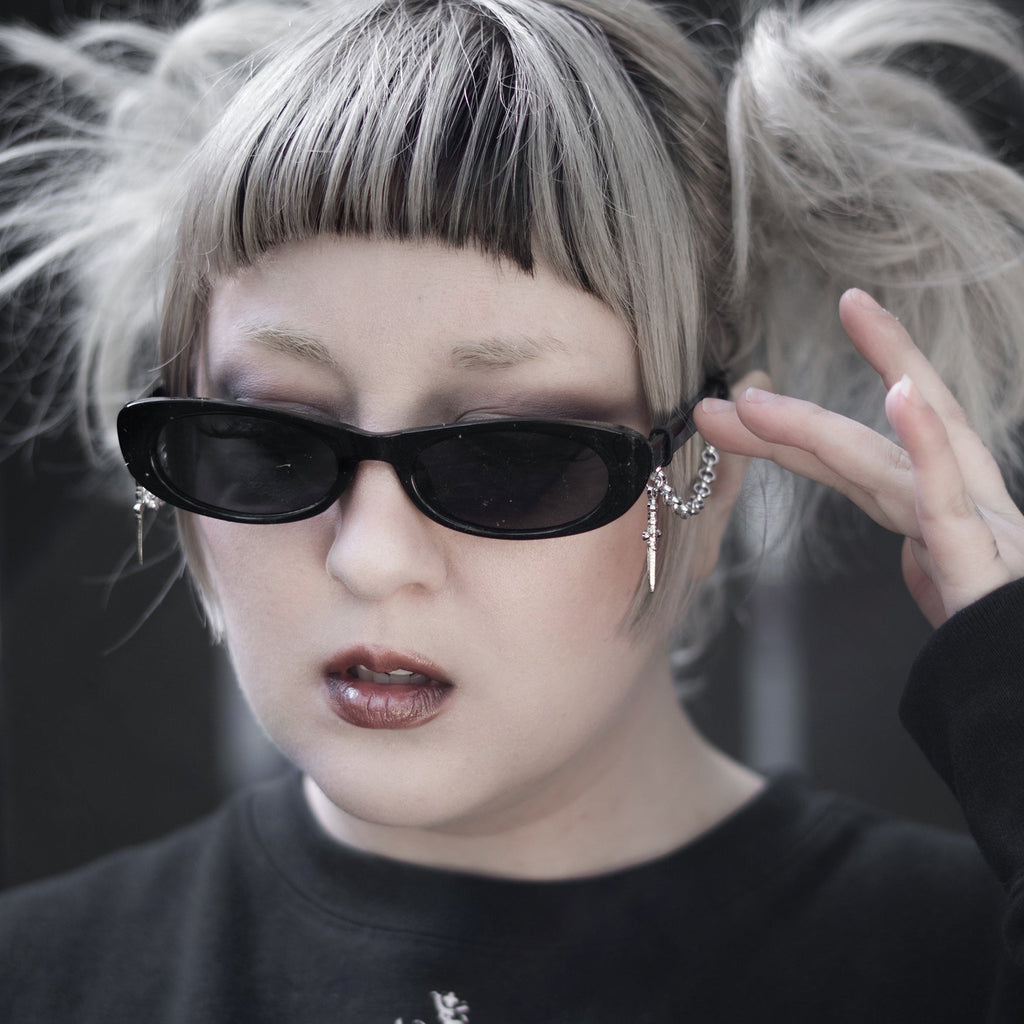 Person with styled hair and sunglasses wearing a black sweater with a heart design.
