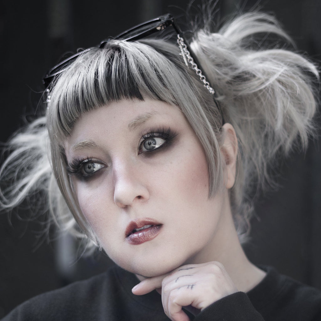 Person with styled hair and dark makeup wearing a black sweater with a heart design.