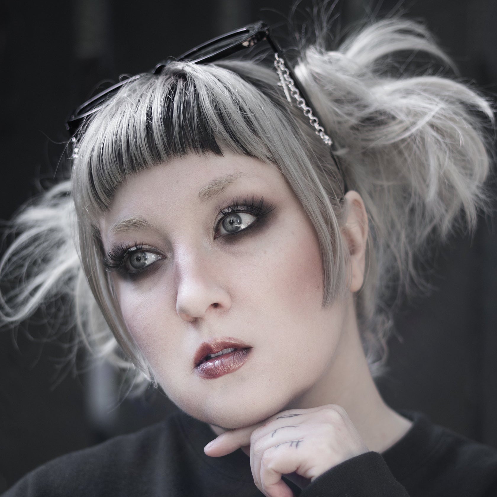 Person with styled hair and dark makeup wearing a black sweater with a heart design.