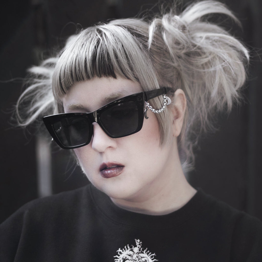 Person wearing black sunglasses and a black sweatshirt with a white design, against a dark background