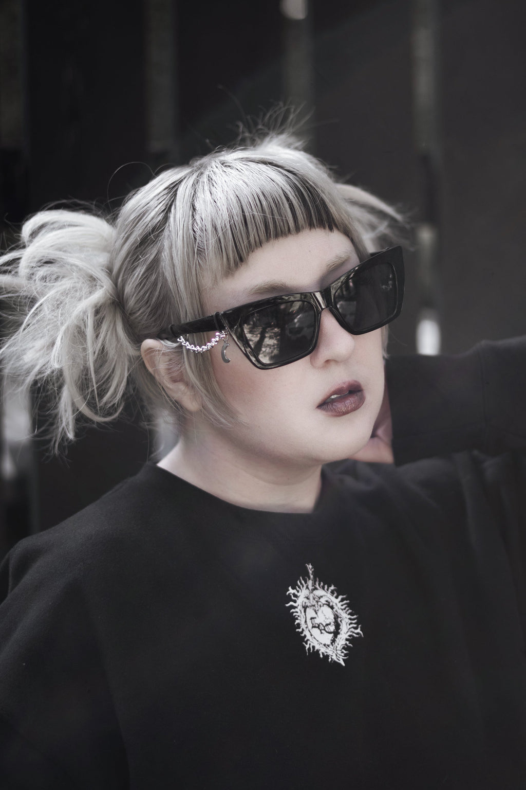 Person wearing sunglasses and a black sweatshirt with a logo, against a dark background