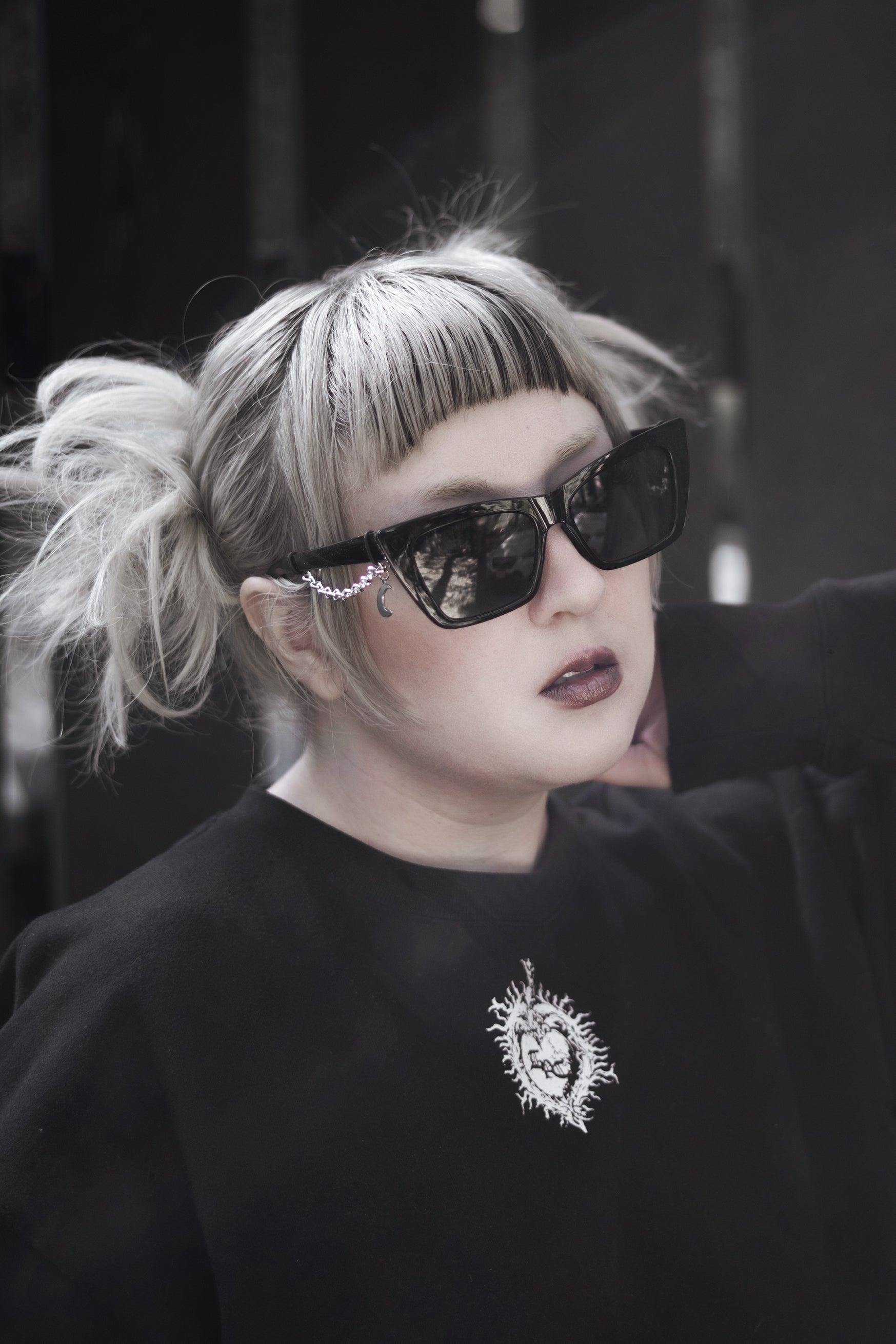 Person wearing sunglasses and a black sweatshirt with a logo, against a dark background