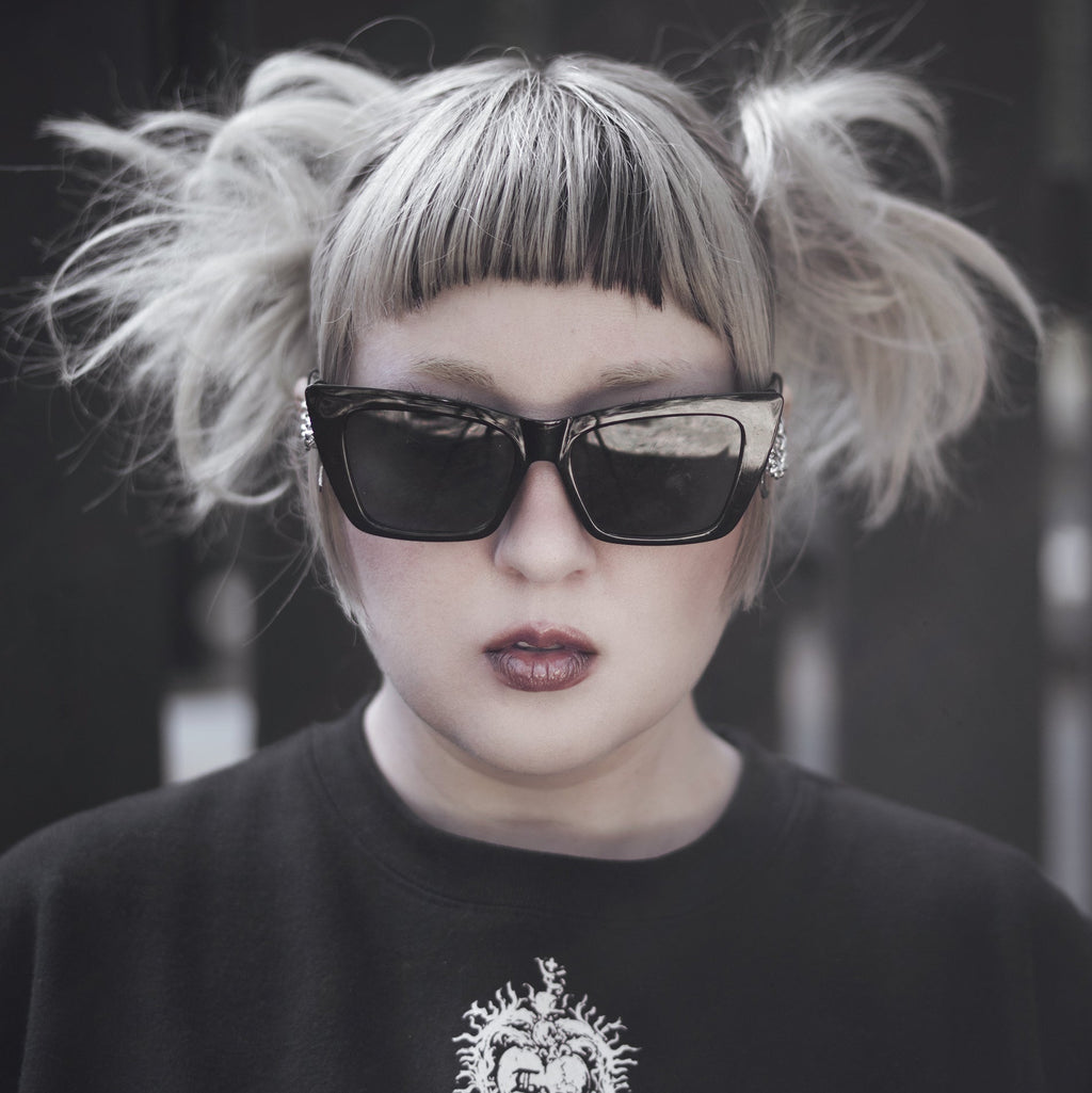 Person with styled hair and sunglasses wearing a black shirt with a heart design.