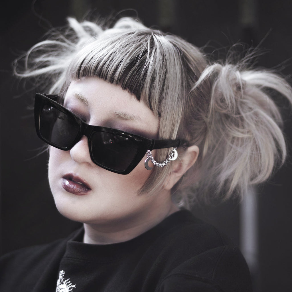 Person wearing black sunglasses and a black outfit with a blurred background