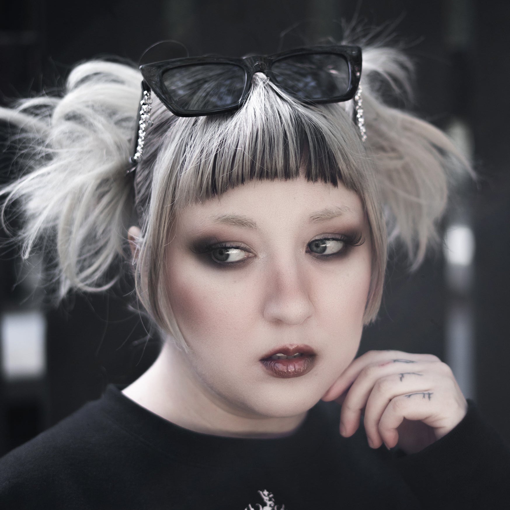Person with styled hair and dark makeup wearing a black sweater with a white design.