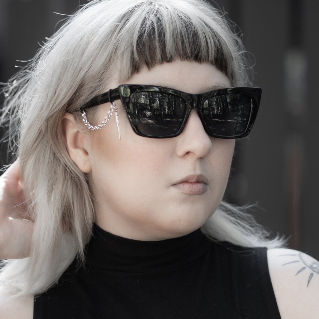 Person with silver hair and black sunglasses wearing a black sleeveless top with a white design.