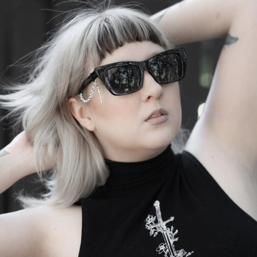 Person wearing black sunglasses and a black turtleneck with a white design.