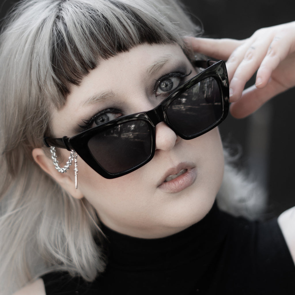 Person wearing black sunglasses and a black sleeveless top with a floral design.