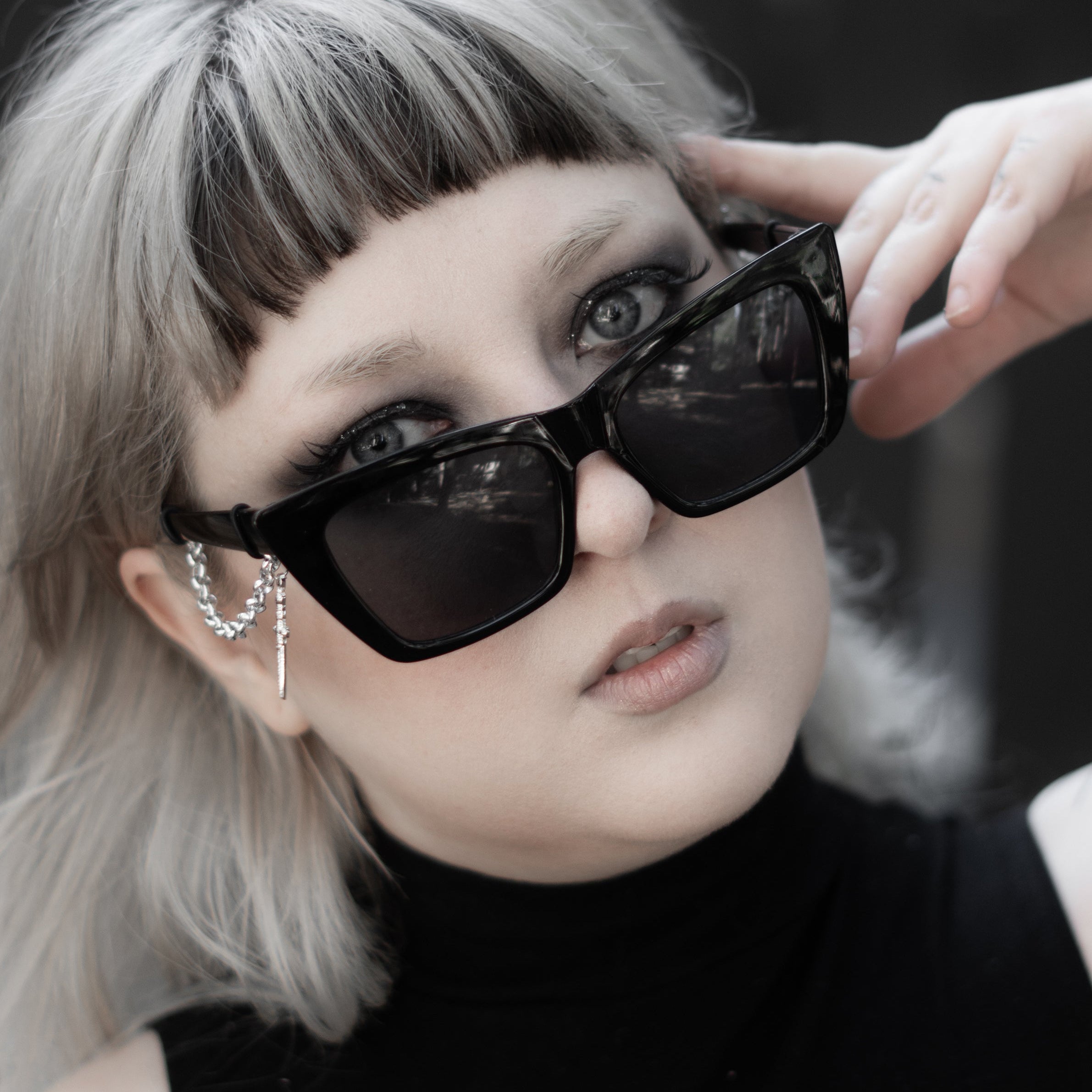 Person wearing black sunglasses and a black sleeveless top with a floral design.