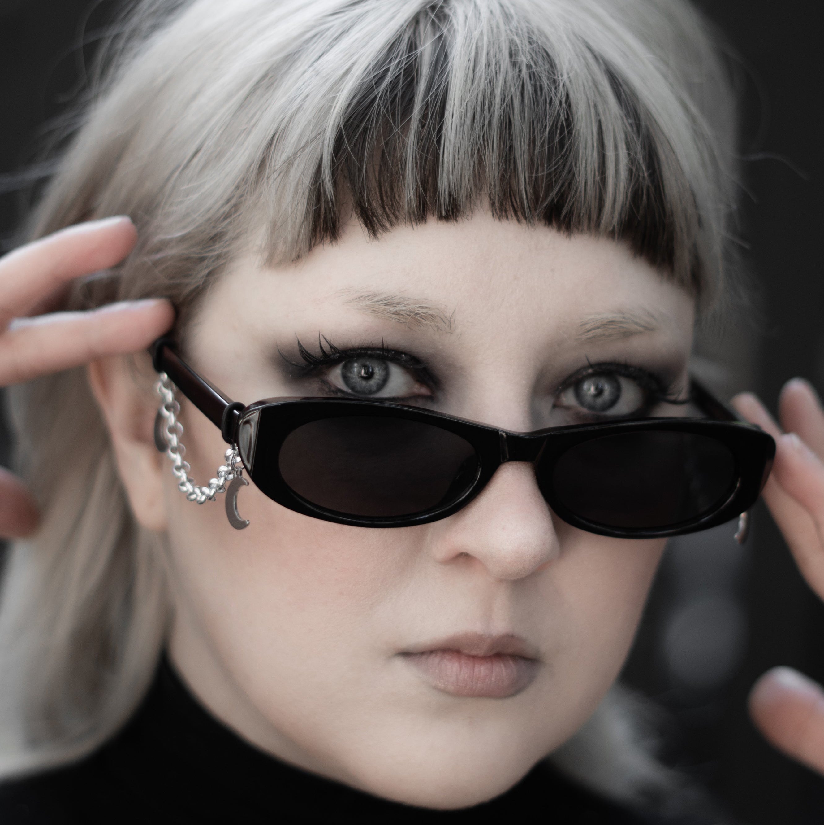 Person with sunglasses and unique hairstyle against a dark background