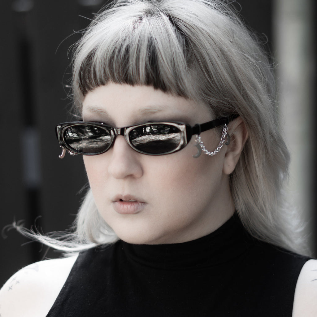 Person with silver hair and sunglasses wearing a black sleeveless top with a white design.