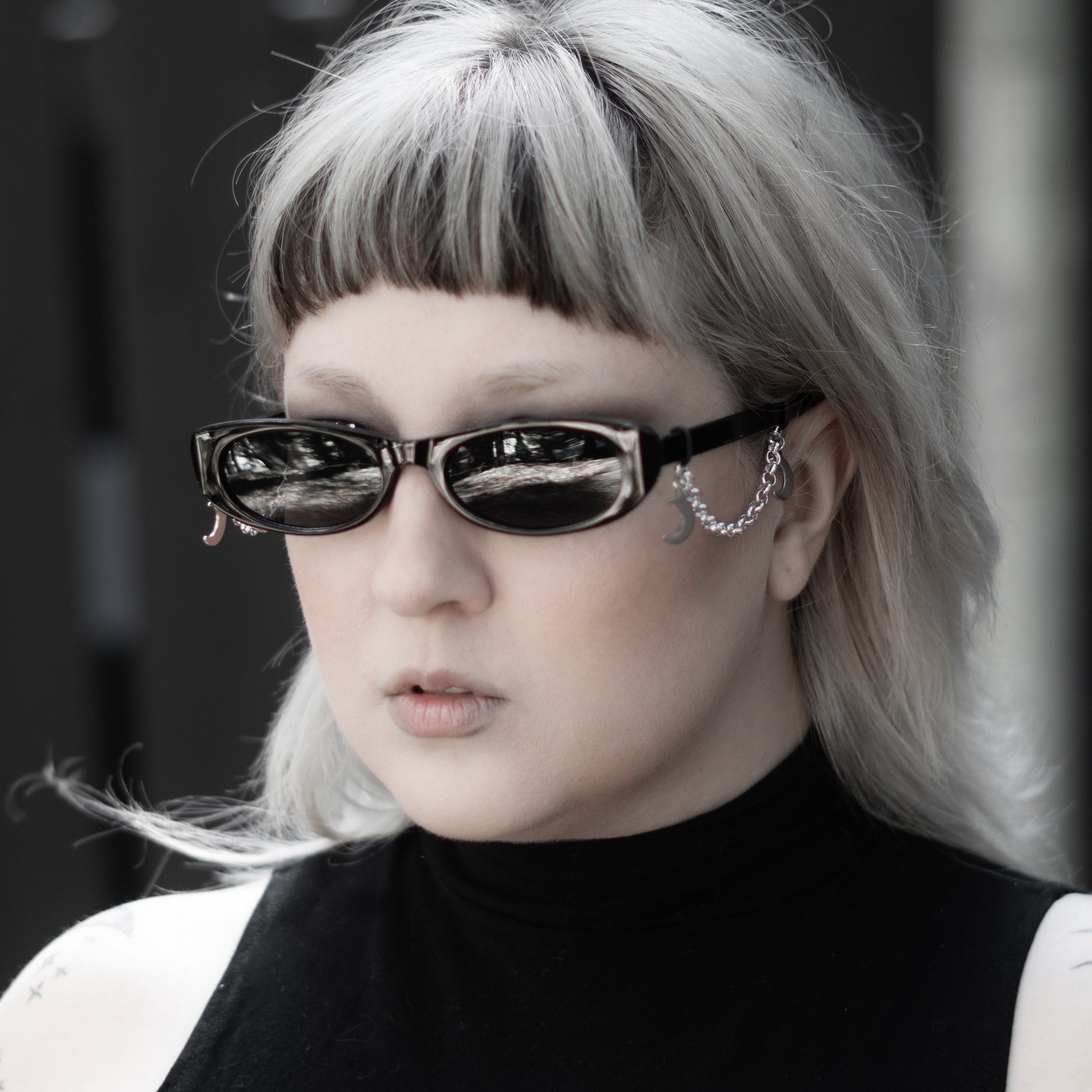 Person with silver hair and sunglasses wearing a black sleeveless top with a white design.
