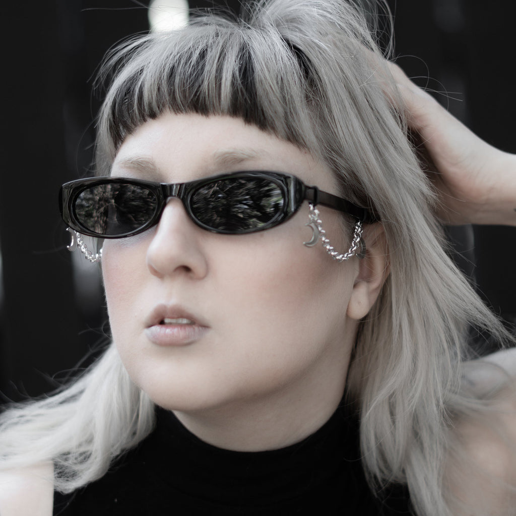 Person with silver hair and black sunglasses wearing a black sleeveless top with a white design.