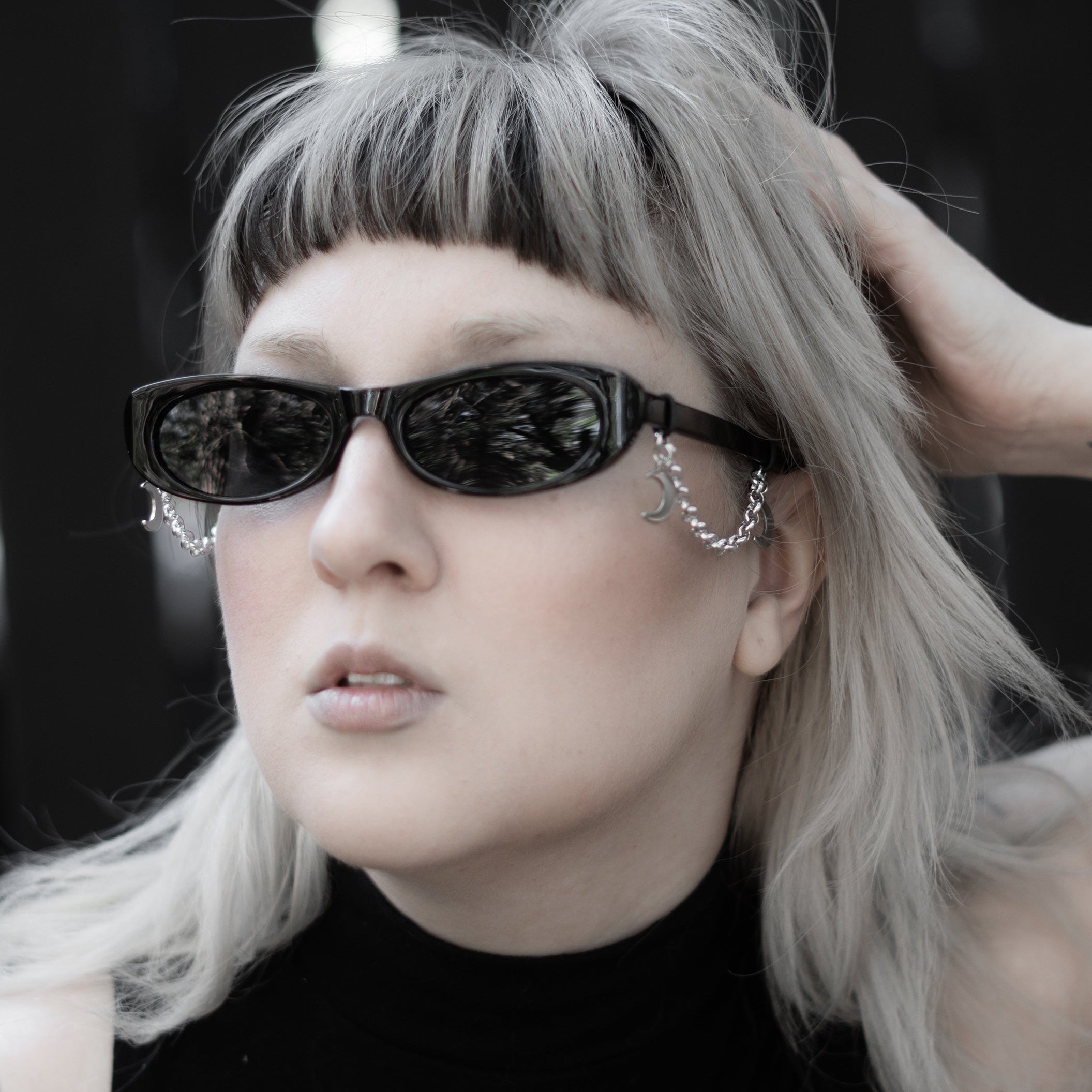 Person with silver hair and black sunglasses wearing a black sleeveless top with a white design.