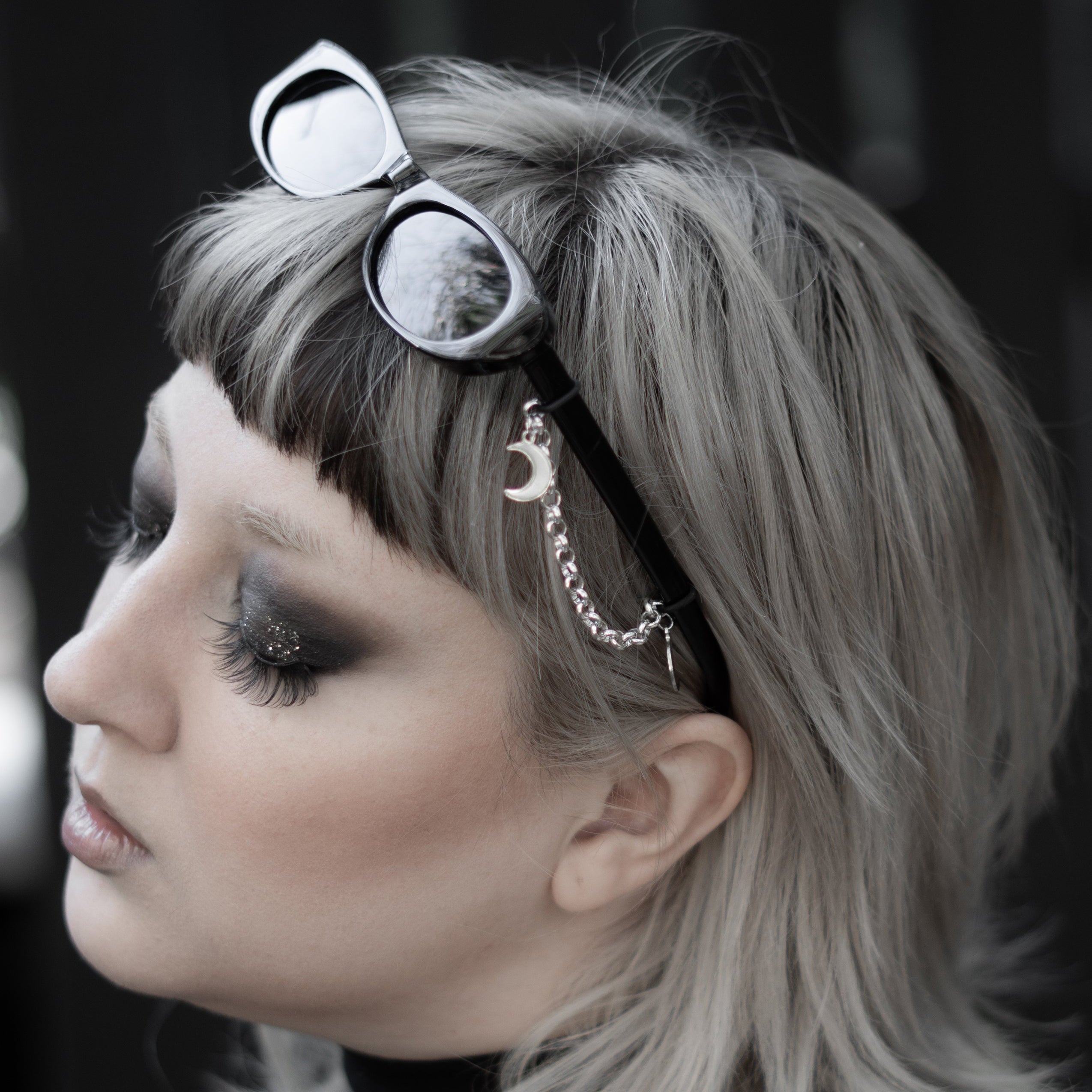 Person with sunglasses on headband and tattoos on neck against a dark background