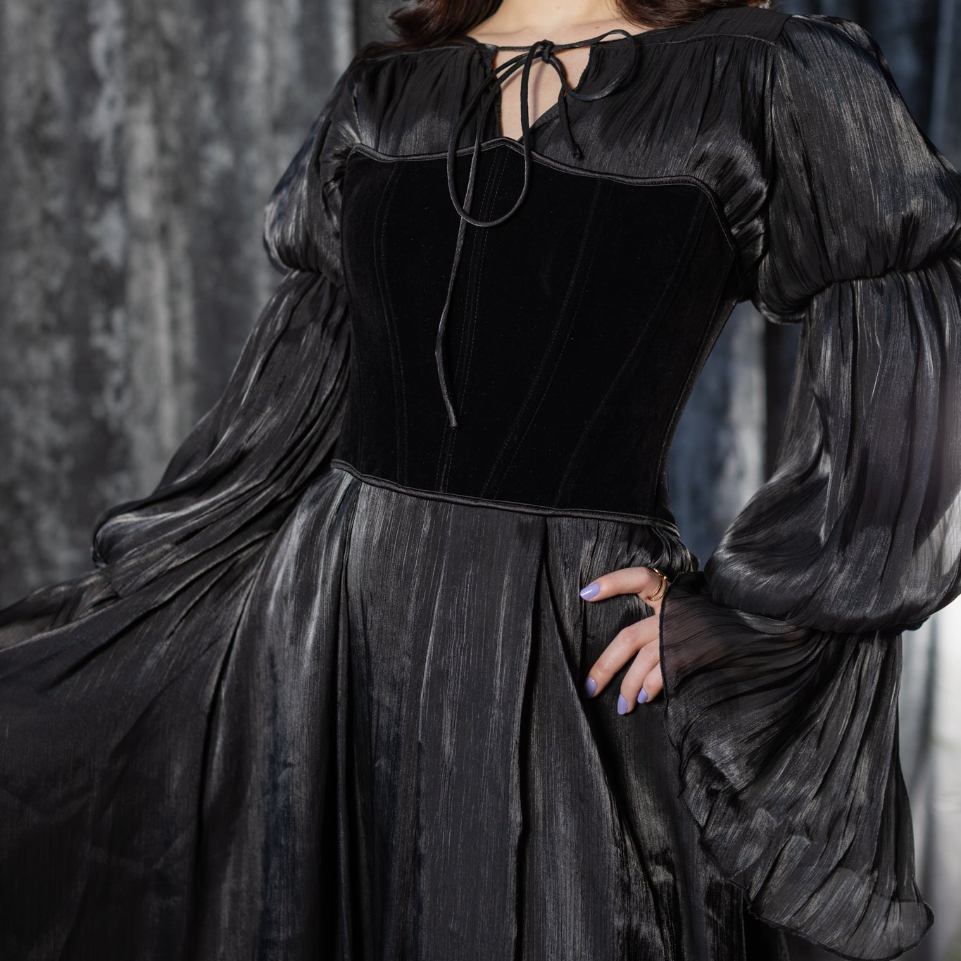 Woman wearing a black dress with long sleeves against a gray curtain background