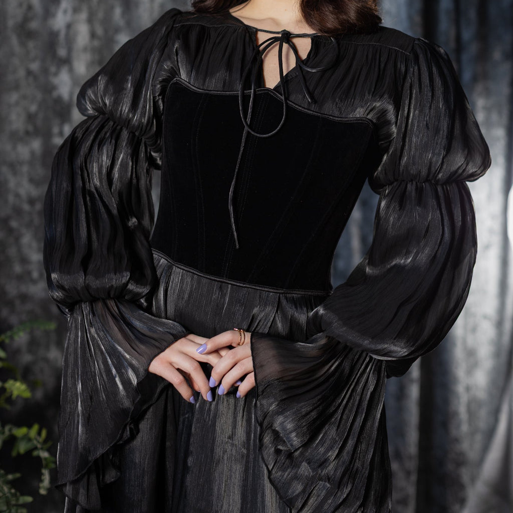 Woman wearing a black dress with puffed sleeves against a dark curtain background